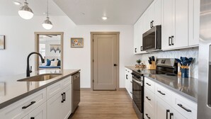 A modern kitchen with white cabinets, stainless steel appliances, and a wooden floor.