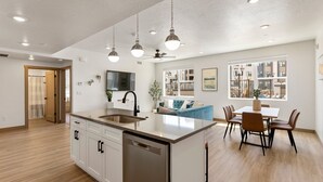 A modern kitchen with a central island, a dining area with a table and chairs, and a view of the city through large windows.