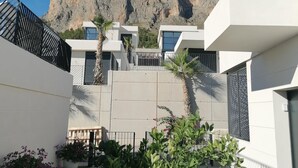 Un bâtiment moderne avec une vue sur les montagnes, caractérisé par un toit plat, de grandes fenêtres et une cour pavée agrémentée de plantes en pot.