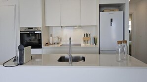 Une cuisine moderne avec des armoires blanches, un four encastré, un évier et un réfrigérateur.