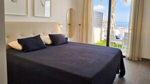 Une chambre d’hôtel moderne avec un grand lit, un balcon donnant sur la plage et un grand miroir.