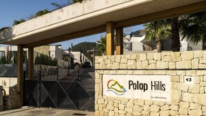 Une entrée fermée par un portail donne accès à un quartier résidentiel appelé Polop Hills, caractérisé par un mur en pierre et un panneau portant un logo.