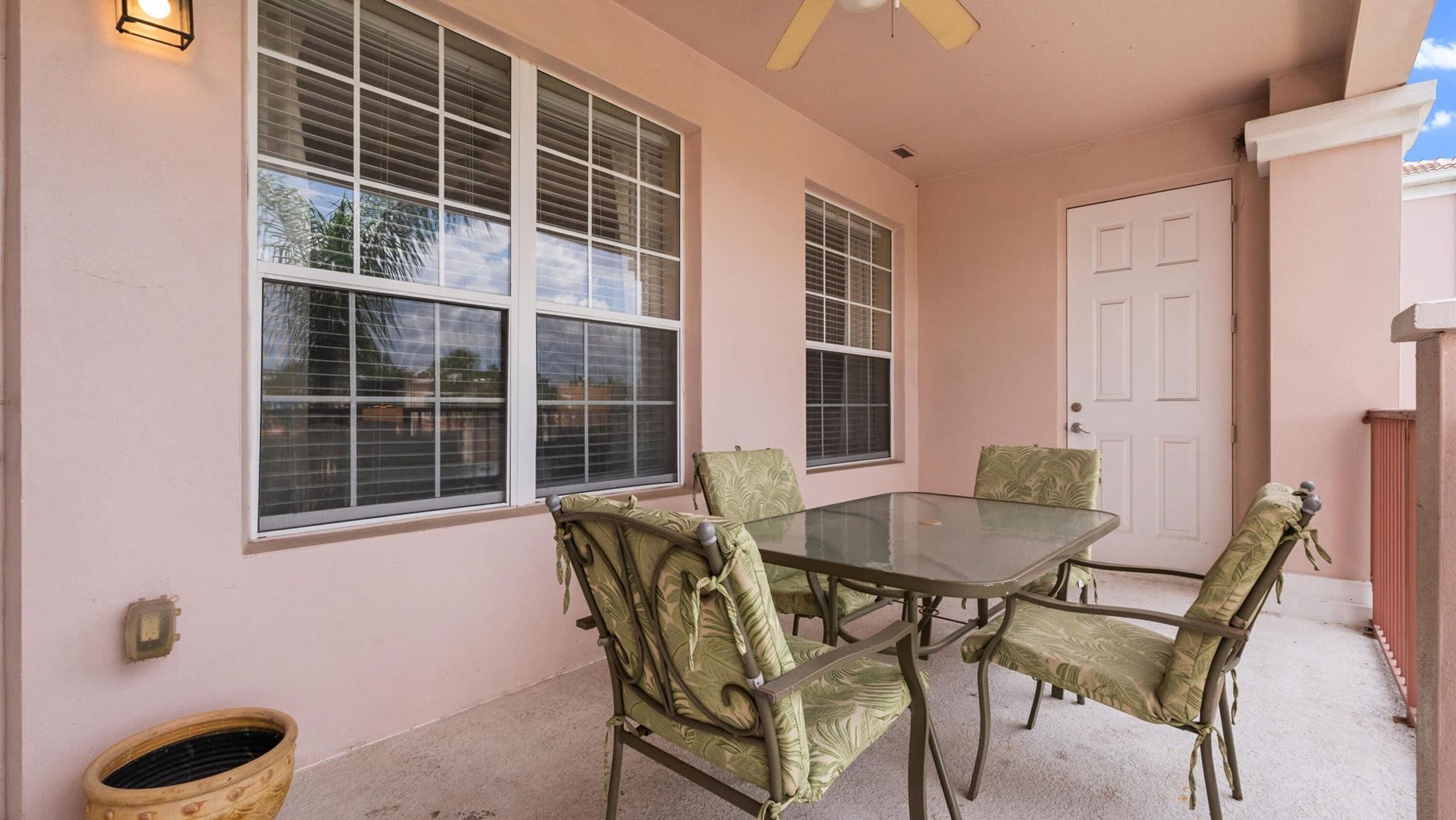 A covered patio with a glass table and four chairs, a white door, and a window with blinds.