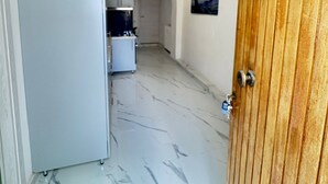 Un pasillo con piso de mármol que conduce a una zona de cocina con gabinetes blancos y un refrigerador.