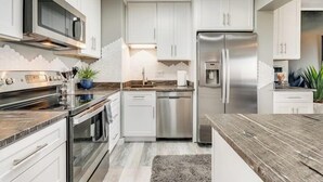 A modern kitchen with white cabinets, stainless steel appliances, and a wooden countertop.