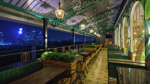 Een restaurant met terras, groen bekleden zitjes en uitzicht over de stad 's nachts.