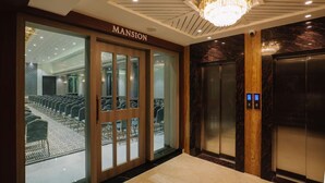 Een hotel lobby met een receptiebalie, een kroonluchter, een lift en een zithoek met stoelen.