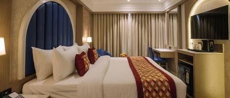 A hotel room with a bed, a desk with a telephone, a television, and a kitchenette area.