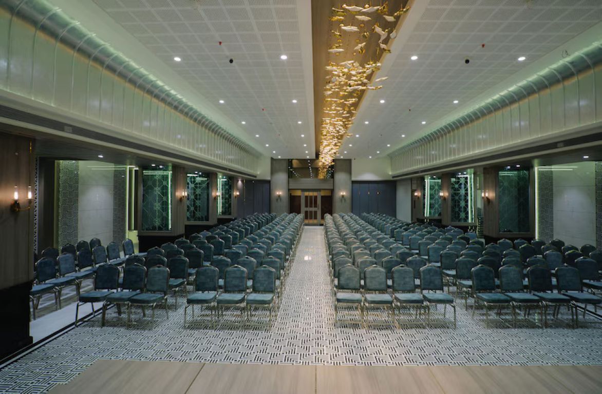 A large conference room with rows of chairs, a patterned floor, and a ceiling with a light fixture.