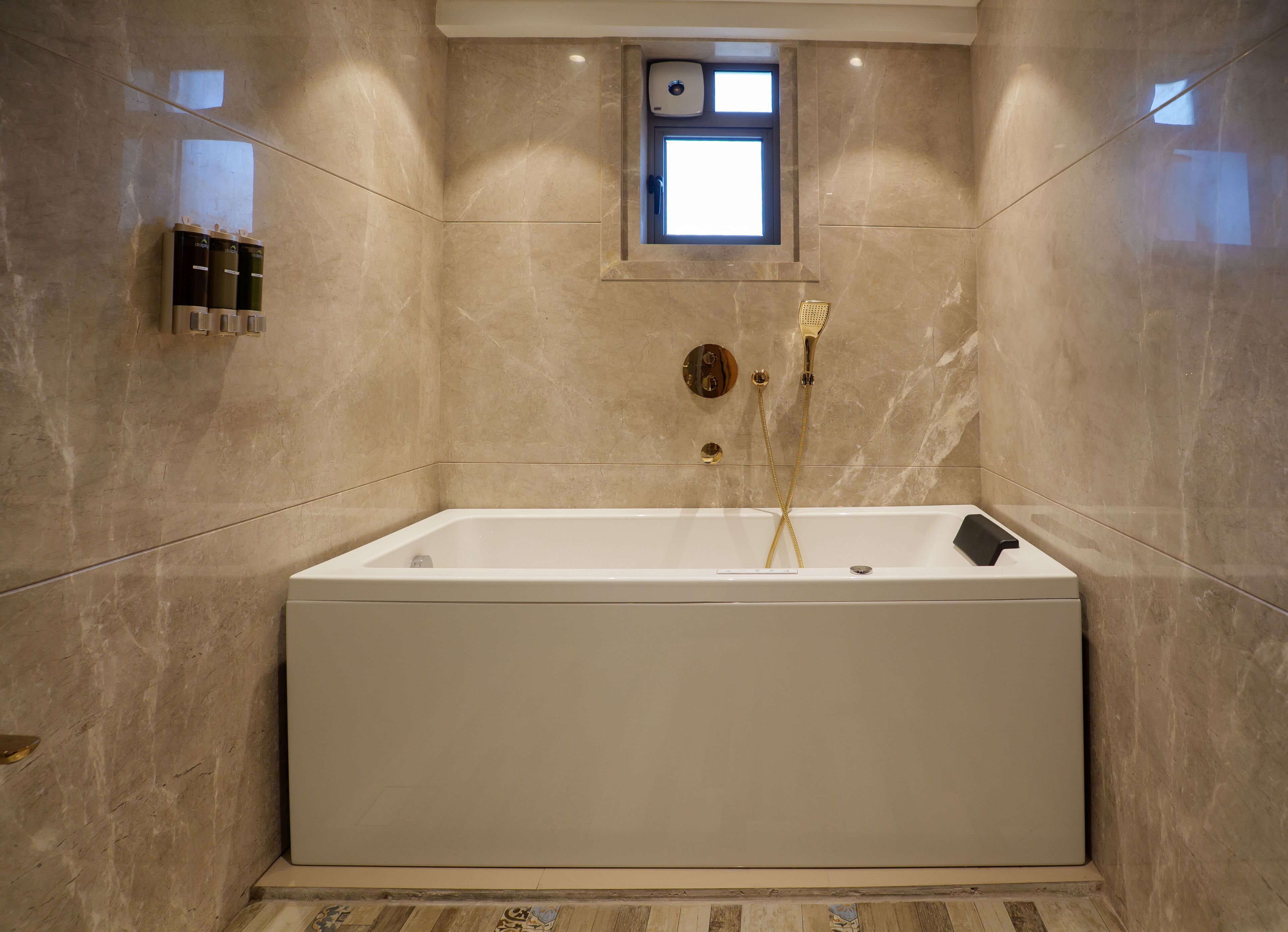 A modern bathroom with a large bathtub, a small window, and a wall-mounted hand dryer.