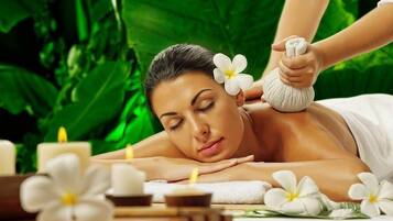 Una persona recibiendo un masaje con flores y velas en un spa.