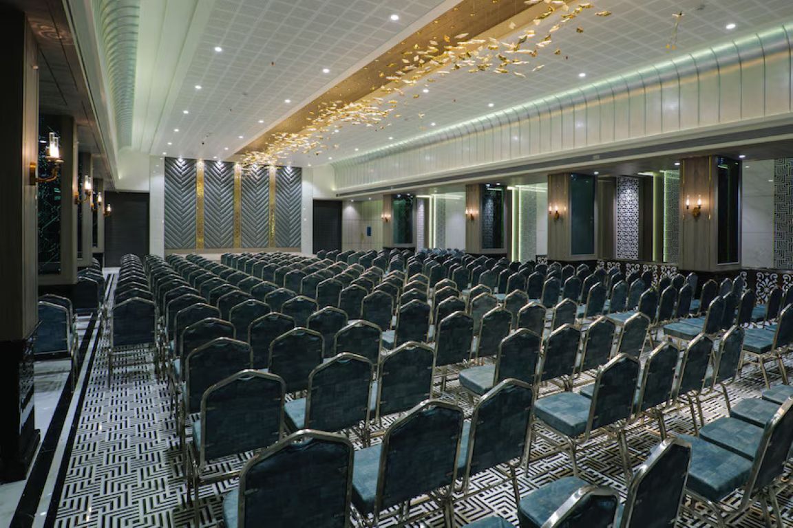 A conference room with rows of chairs, a patterned floor, and a ceiling with hanging lights.