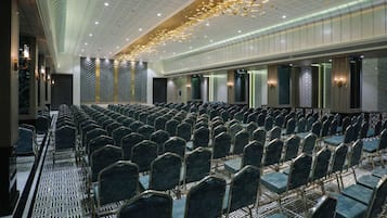 A conference room with rows of chairs, a patterned floor, and a ceiling with hanging lights.