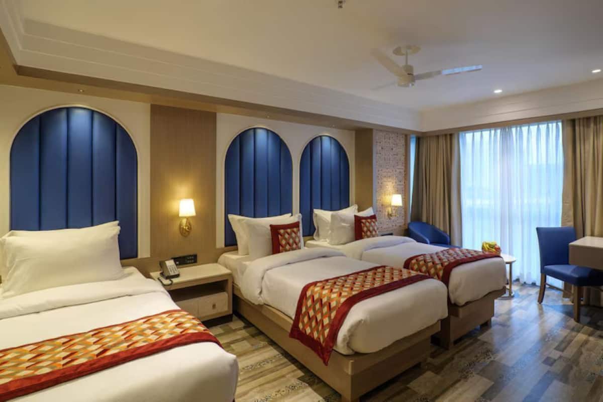 A hotel room with three beds, a desk, a chair, and a view of the city.