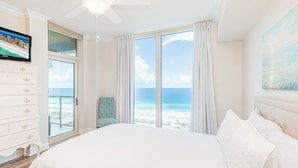 A bedroom with a large bed, a ceiling fan, a TV, a dresser, and a view of the beach. - Exquisite 2B Gulf View Condo at Portofino 4-2006 (Pensacola Beach)