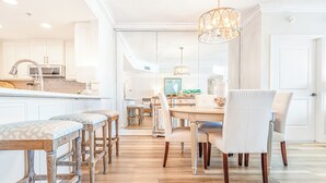 A modern kitchen with white cabinetry, a wooden island with bar stools, and a dining area with a round table and chairs. - Exquisite 2B Gulf View Condo at Portofino 4-2006 (Pensacola Beach)