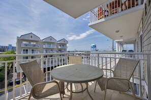 Un balcon doté d’une table ronde et de chaises en osier, offrant une vue sur un quartier résidentiel avec des immeubles à plusieurs étages et un château d’eau.