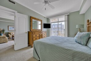 Une chambre à coucher comprenant un lit, une commode, un téléviseur et une fenêtre donnant sur des immeubles.