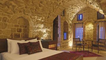 A stone-walled bedroom with a large bed, two chairs, and a small table.
