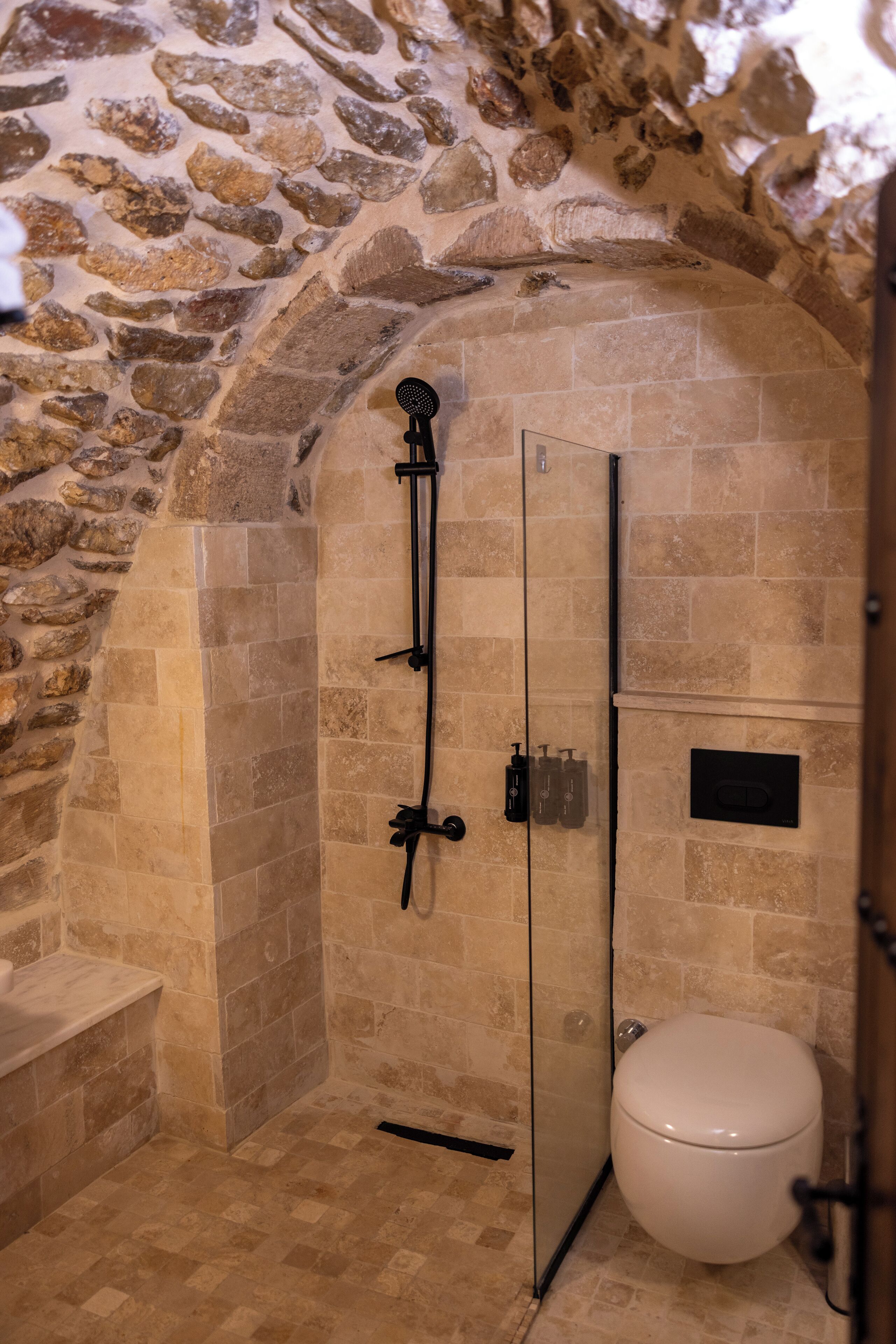 A bathroom with a stone wall, a glass shower enclosure, and a toilet.