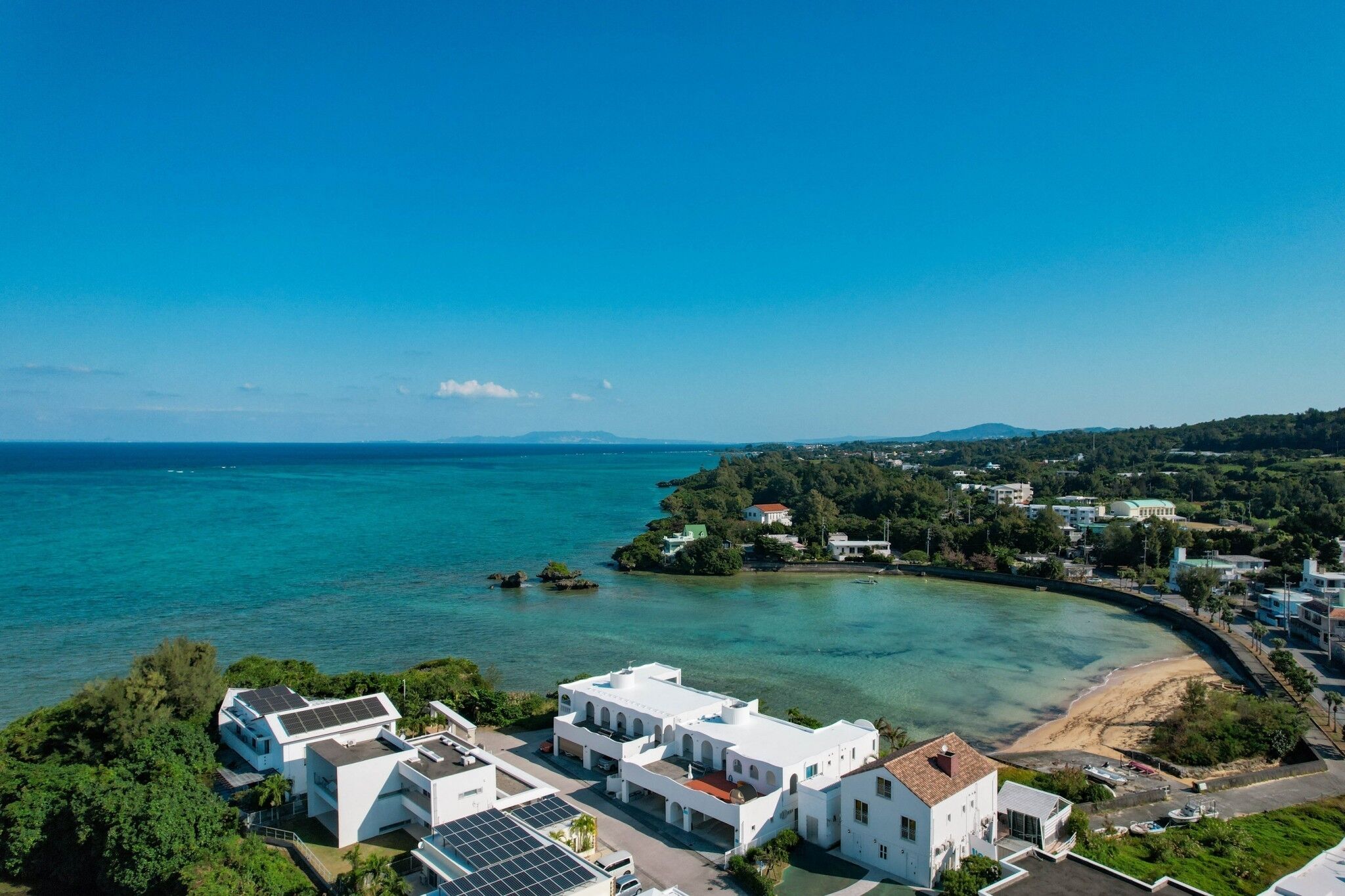 A coastal town with modern buildings, a beach, and clear blue waters.