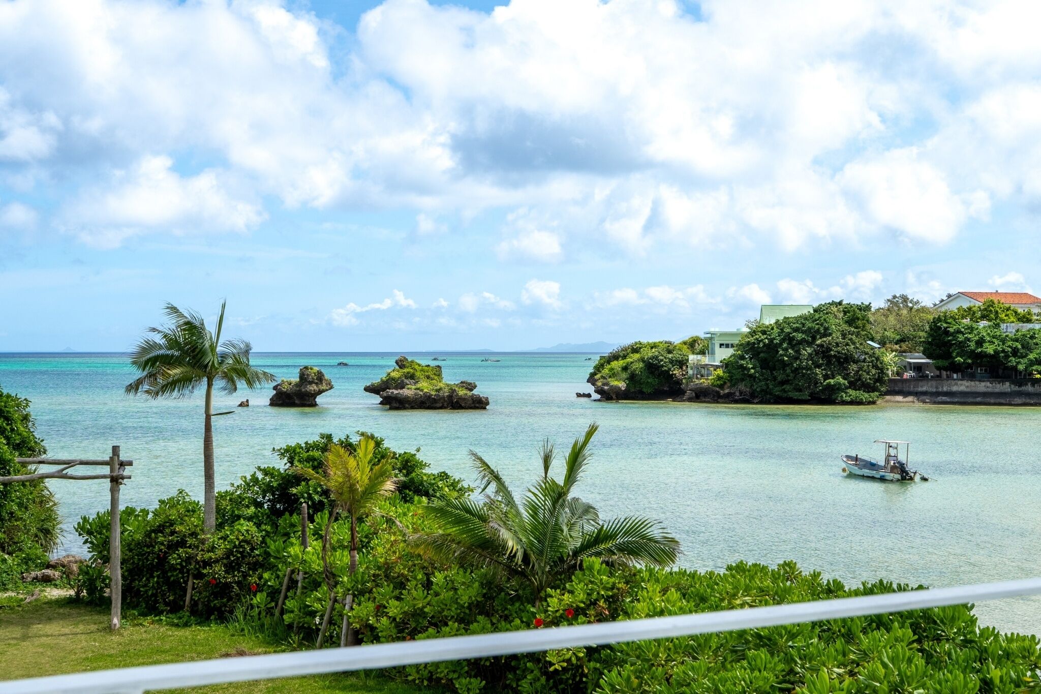 Vista costera tropical con cielos despejados, un barco pequeño y exuberante vegetación.