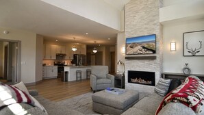 A spacious living room with a fireplace, a kitchen in the background, and a large TV mounted on the wall. - Spacious condo centrally located in Silverthorne! (Silverthorne)