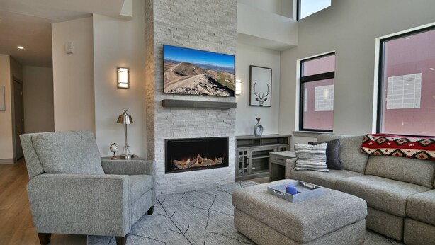 A modern living room with a fireplace, grey sofas, a coffee table, and a large TV mounted on the wall. - Spacious condo centrally located in Silverthorne! (Silverthorne)