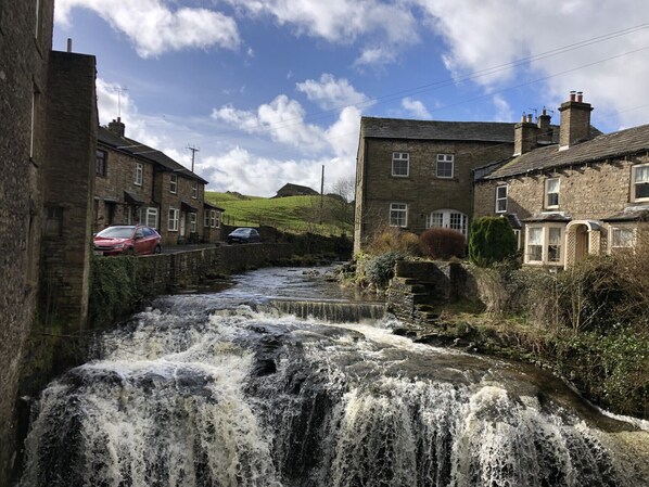 A historic stone building with a traditional design, a narrow water channel, and a red car parked nearby. - Logburner / Inglenook Fireplace. Dogs Welcome, By A Great Pub & The Pennine Way. (Hawes)