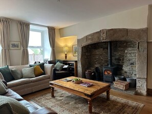 A cozy living room with a stone fireplace, a sofa, a coffee table, and a lamp. - Logburner / Inglenook Fireplace. Dogs Welcome, By A Great Pub & The Pennine Way. (Hawes)