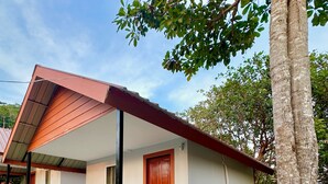 Une maison de plain-pied avec un toit rouge, un balcon doté d’une balustrade noire et une porte avec un cadre rouge.
