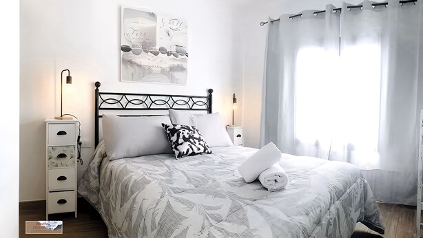 A neatly made bed with a patterned bedspread, a bedside lamp, a white nightstand with drawers, and a wall-mounted picture. - Apartment Alegranza in the Beautiful Village of Mozaga, Lanzarote (Teguise)