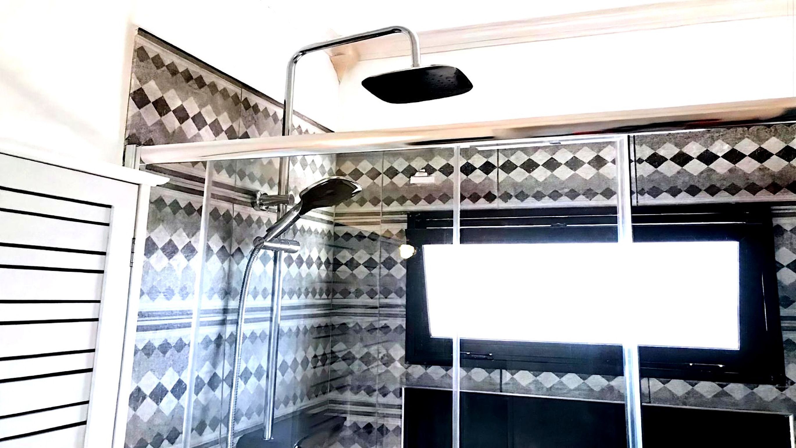 Ein Duschbereich mit modernem Design, gekennzeichnet durch eine Wand mit geometrischem Muster und eine klare Glaseinfassung.