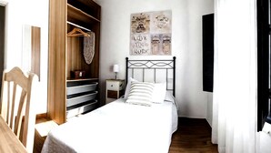 A bedroom with a bed, a nightstand, a wooden wardrobe, and a wall with artwork. - Apartment Alegranza in the Beautiful Village of Mozaga, Lanzarote (Teguise)