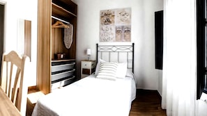 A bedroom with a bed, a nightstand, a dresser with open shelves, and a wall with decorative art. - Apartment Alegranza in the Beautiful Village of Mozaga, Lanzarote (Teguise)