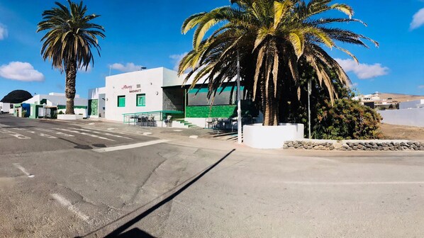 Une vue de rue avec un bâtiment blanc portant l’inscription « BAZARROTT » et des palmiers.