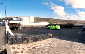 Un área de estacionamiento con un coche verde, un edificio de techo plano y un cielo despejado.