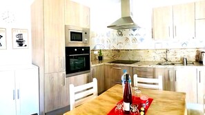 Una cocina con armarios de madera, microondas, horno, lavamanos y una mesa de comedor con sillas.