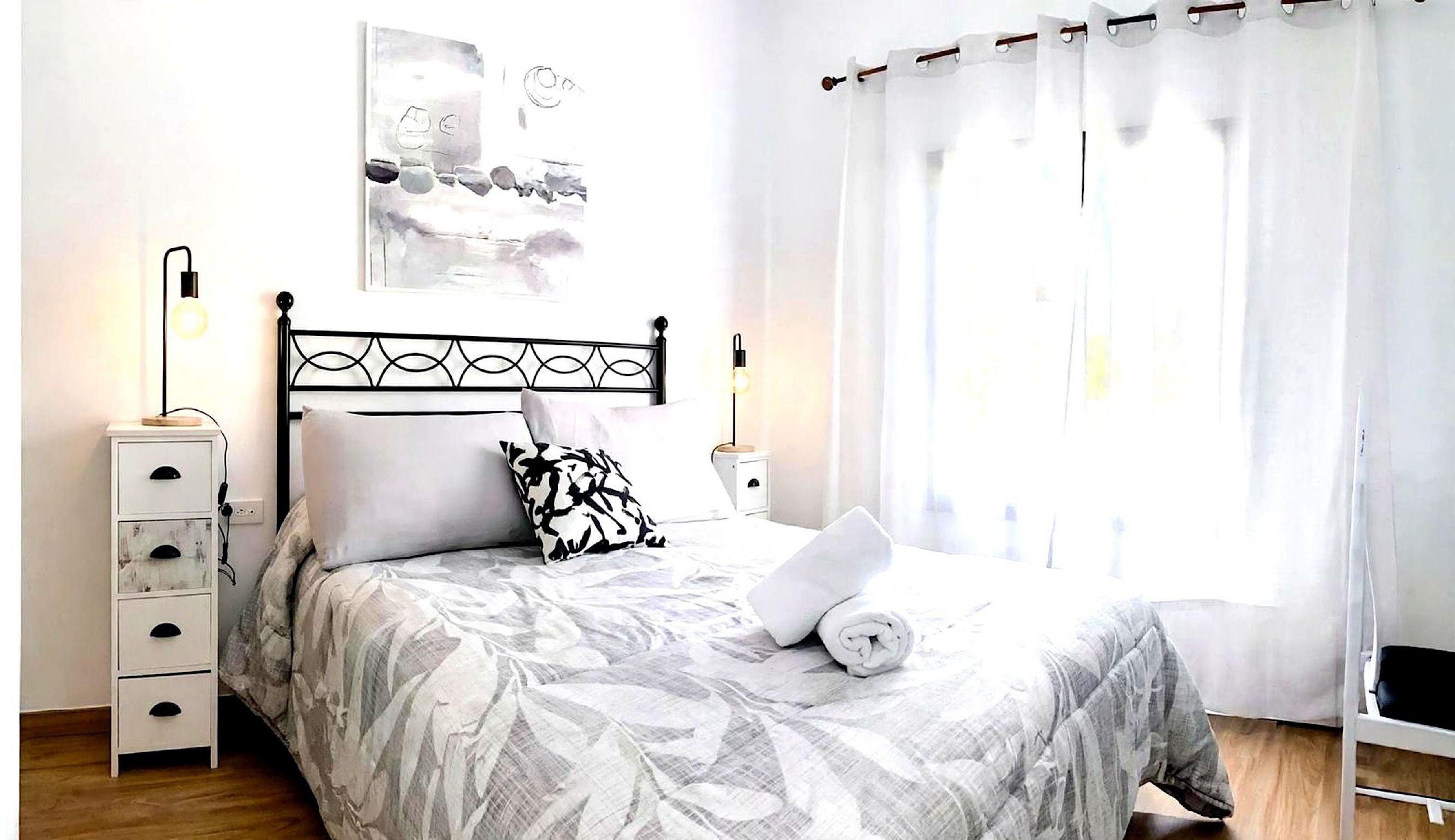 A neatly arranged bedroom with a bed, bedside tables, a lamp, and a window with curtains.