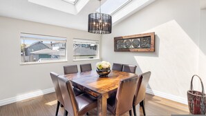 Ein Esszimmer mit Holztisch, sechs Stühlen, einer Chandelier und zwei Fenstern mit Blick auf Häuser.