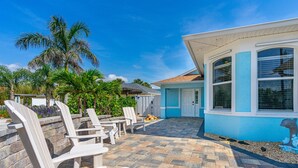 A house with a blue exterior, a patio with stone tiles, and several white lounge chairs. - Dog Friendly and STEPS from the Ocean! Big Beach House with Pool, BBQ & Garage (New Smyrna Beach)