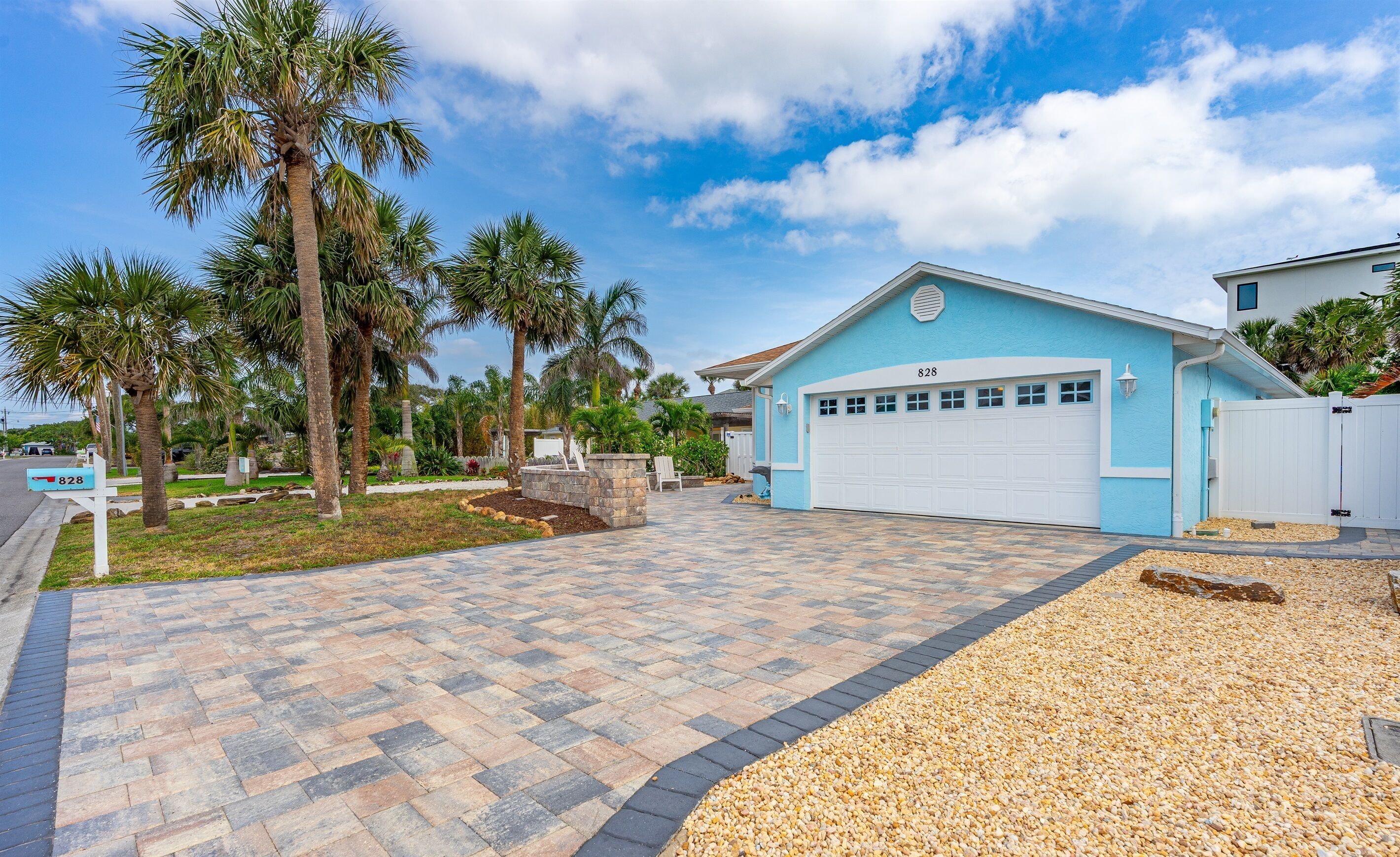 A residential property with a blue garage, palm trees, and a paved driveway.