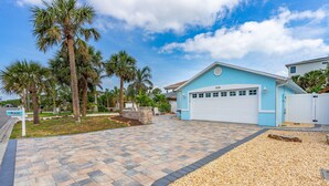 A residential property with a blue garage, palm trees, and a paved driveway. - Dog Friendly and STEPS from the Ocean! Big Beach House with Pool, BBQ & Garage (New Smyrna Beach)