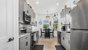 A modern kitchen with stainless steel appliances, white cabinetry, and a dining area with a black table and chairs. - Dog Friendly and STEPS from the Ocean! Big Beach House with Pool, BBQ & Garage (New Smyrna Beach)