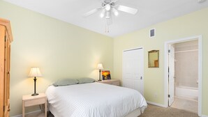 Un dormitorio con cama, dos mesitas de noche con lámparas, ventilador de techo, puerta y vestidor.