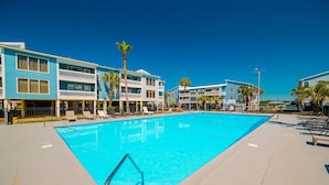 A swimming pool with lounge chairs and a building with balconies. - Sea Oats 105h 3 Bedroom Condo (Gulf Shores)