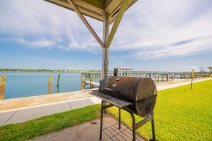 Un espacio de parrilla al aire libre techado con vista a un cuerpo de agua y un muelle distante.