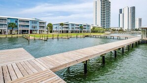 A waterfront property with a wooden dock extending into the water, surrounded by modern buildings with balconies. - Sea Oats 105h 3 Bedroom Condo (Gulf Shores)