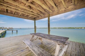 Une terrasse en bois avec une table de pique-nique, une vue dégagée sur l’eau et, au loin, une côte bordée de bâtiments.