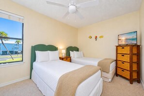 A hotel room with two beds, a ceiling fan, a window with a view of palm trees, and a wall with decorative fish stickers.